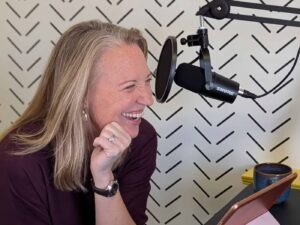 Woman seated at a desk, laughing, in front of a podcast microphone