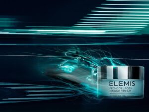 Artistic image of a pot of Elemis skin care cream combined with an F1 racing car against a black and neon green/blue background