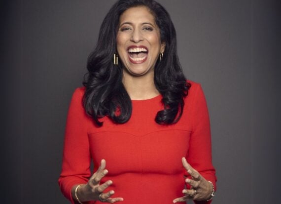 Portrait of Leena Nair wearing a red dress with three quarter length sleeves, laughing against a grey background