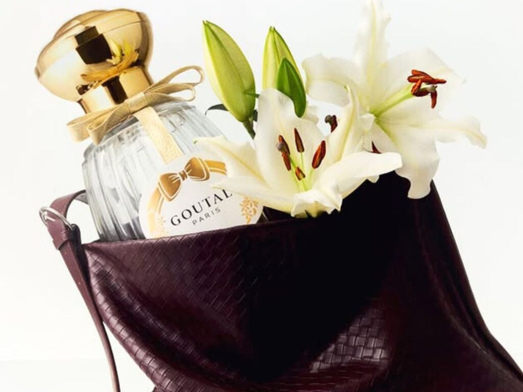 goutalparis Brown leather toe bag open with a bottle of Goutal Paris perfume inside and bunch of Lillies in full bloom