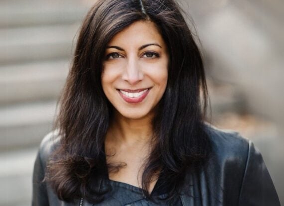 Smita Reddy, wearing a black leather biker style jacket, smiling against the background of blurred street steps