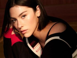 Portrait photo of Gracie Abrams wearing a black and white off the shoulder sweater with red cuffs