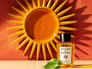 Acqua di Parma bottle with basil leaves and a ceramic warm golden sun on the wall behind it