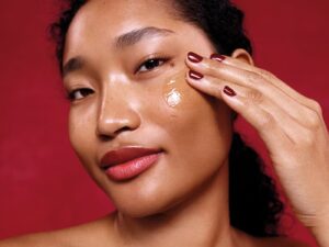 Model applies clear cleansing balm to her cheek, smiling, with red cherry background
