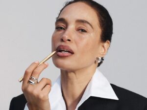 Woman in business suit, with her dark brown hair pulled back, applies lipliner pencil.