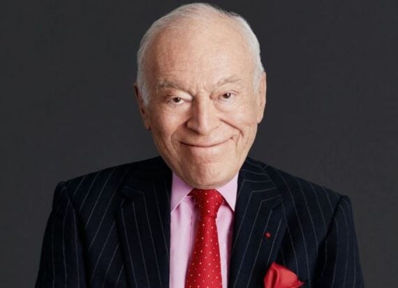Portrait of Leonard A. Lauder, wearing a suit and pale pink shirt, with a red tie with white spots, and a red handkerchief visible in his jacket pocket, smiling.
