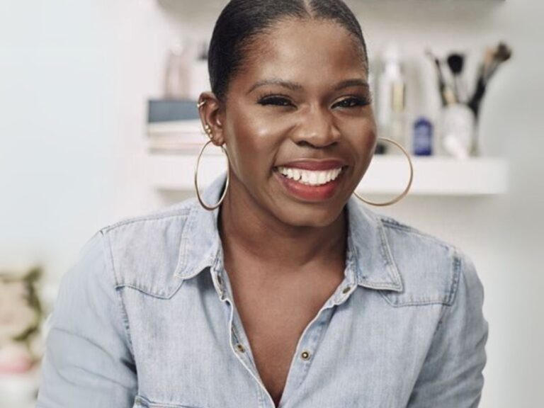 Funmi Fetto smiling, wearing a pale blue denim shirt and large gold hoop earrings