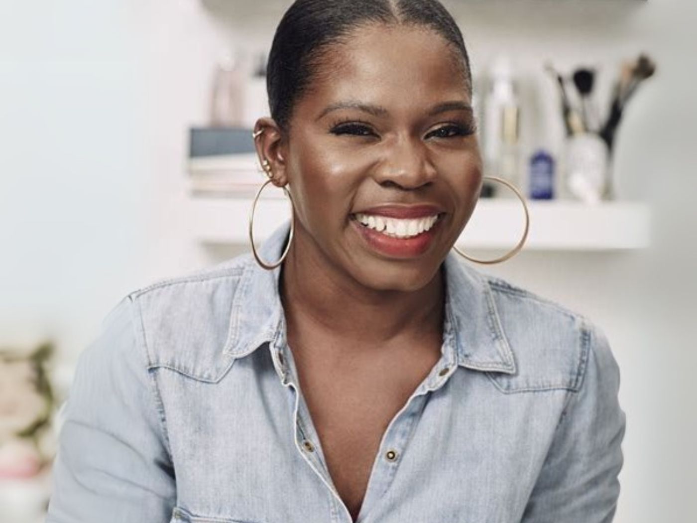 Funmi Fetto smiling, wearing a pale blue denim shirt and large gold hoop earrings