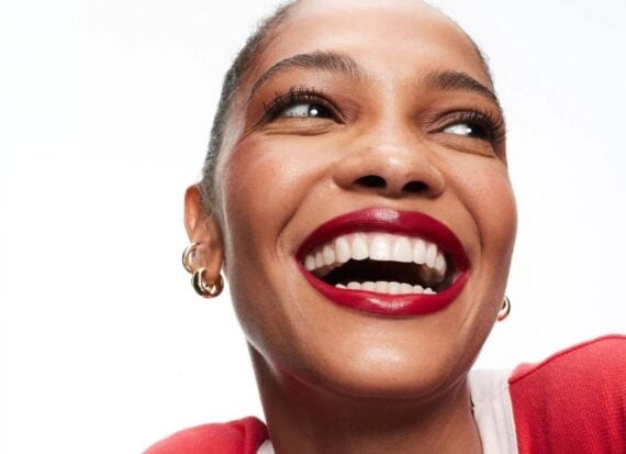 Close up of a young woman smiling wearing bold red lipstick, matching a red and white sweater and wearing gold earrings.