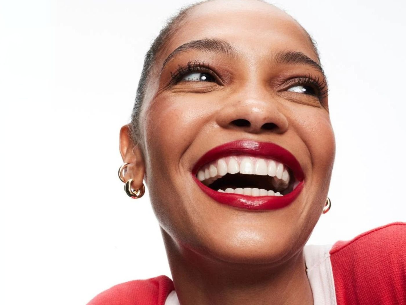 Close up of a young woman smiling wearing bold red lipstick, matching a red and white sweater and wearing gold earrings.