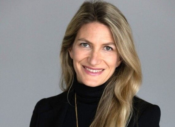 Woman with long blonde hair wearing a black turtleneck sweater and a gold necklace, smiling.