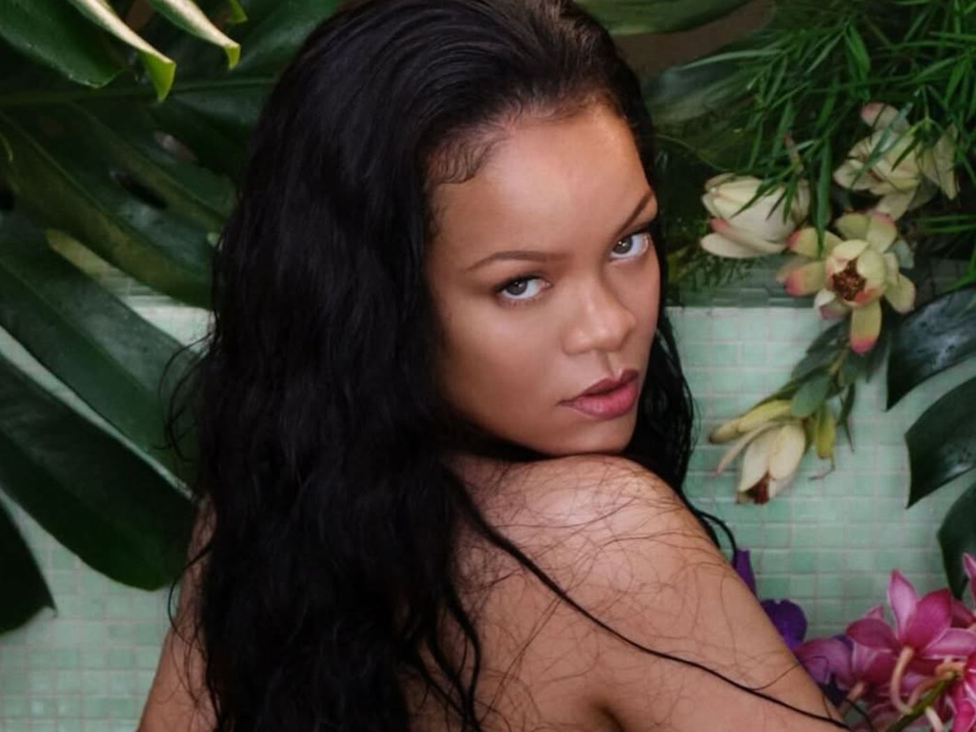 Rihanna looking over her shoulder, with tropical flowers around her.