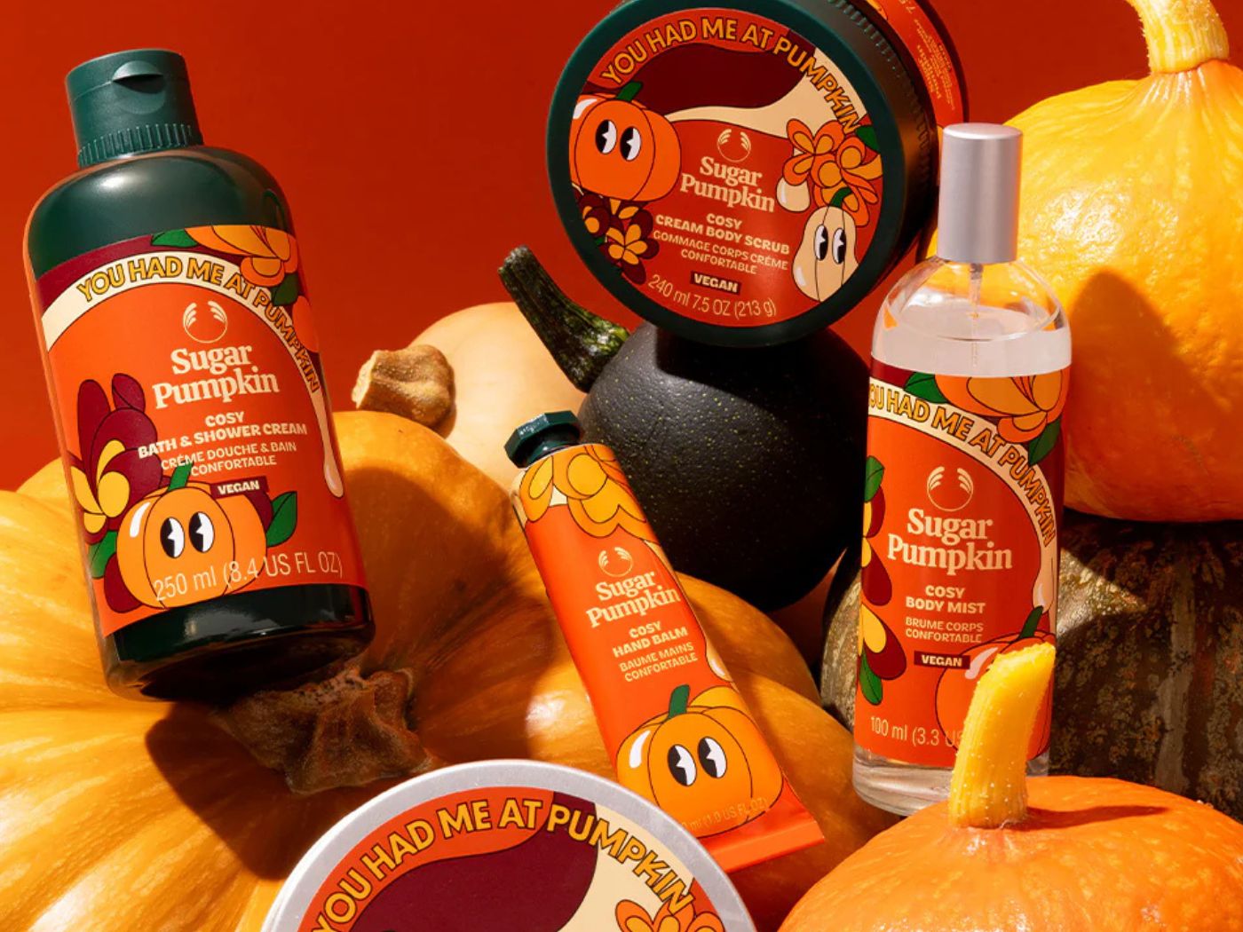 Range of orange colored bath and body care products arranged next to giant orange pumpkins and squashes