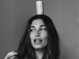 Black and white photo of Hailey Rhode-Beiber, with a Rhode tube of product balanced on her head.