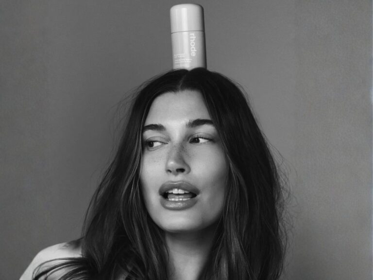Black and white photo of Hailey Rhode-Beiber, with a Rhode tube of product balanced on her head.