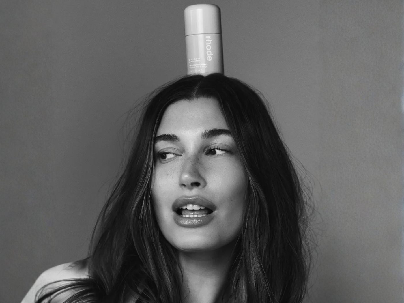 Black and white photo of Hailey Rhode-Beiber, with a Rhode tube of product balanced on her head.