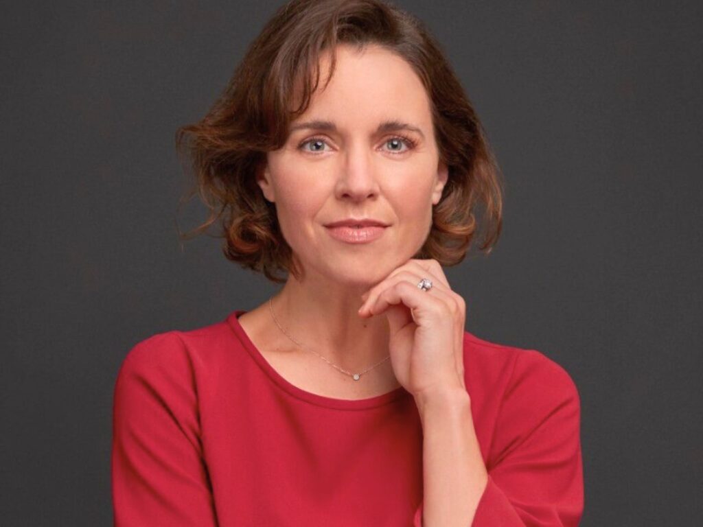 Woman in a red dress, resting her hand on her chin, smiliing