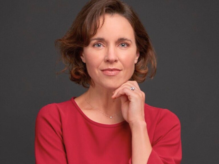 Woman in a red dress, resting her hand on her chin, smiliing