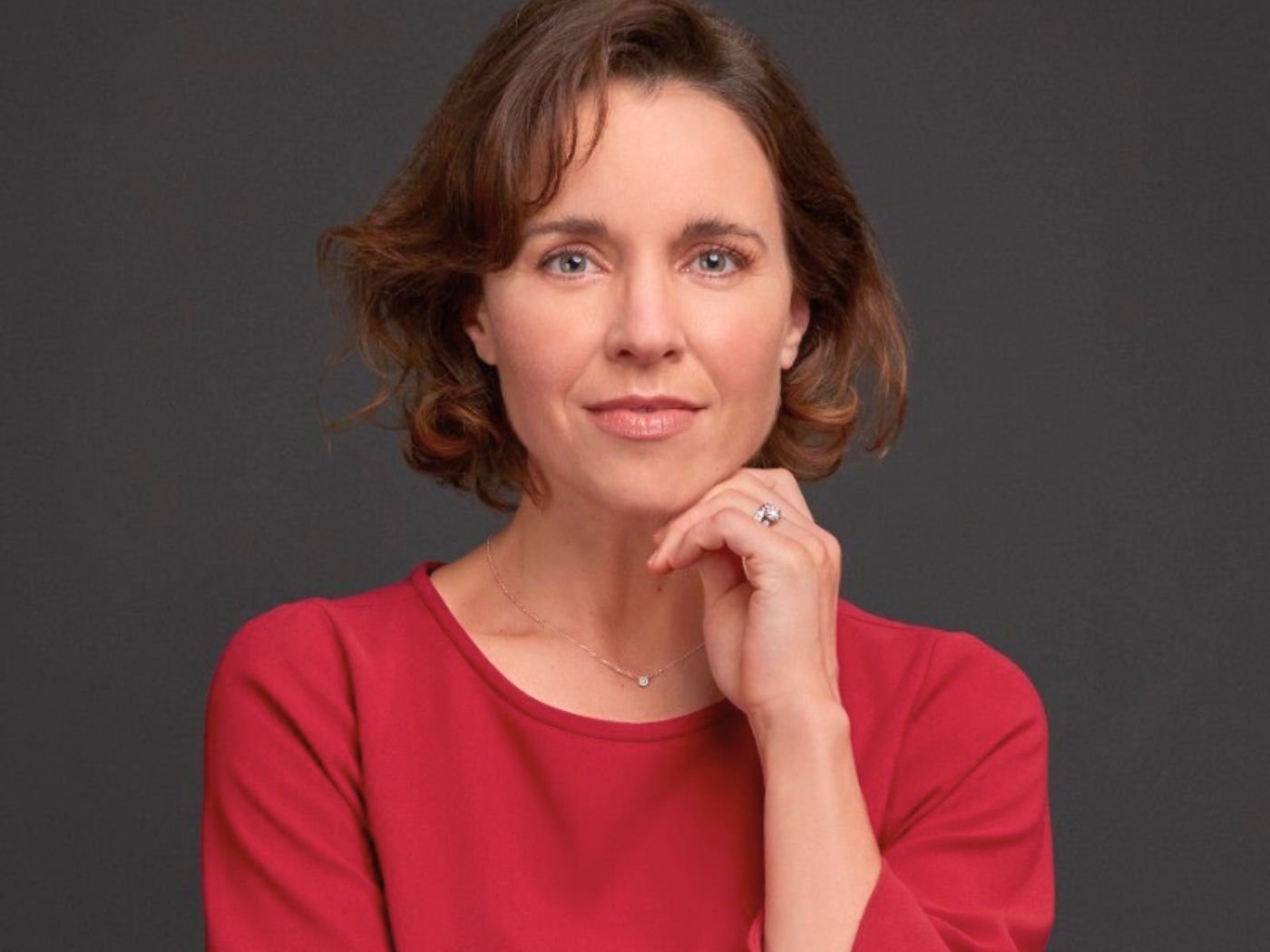 Woman in a red dress, resting her hand on her chin, smiliing