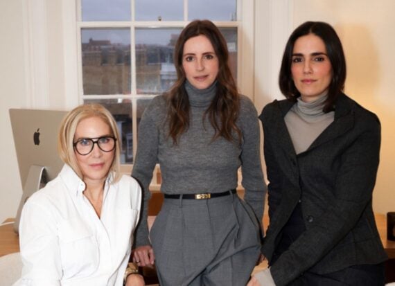 Veronika Ullmer, Clare Goodwin and Jessica Diner. Three women side by side at a desk, in an office by the window, with an Apple desktop computer in the background.